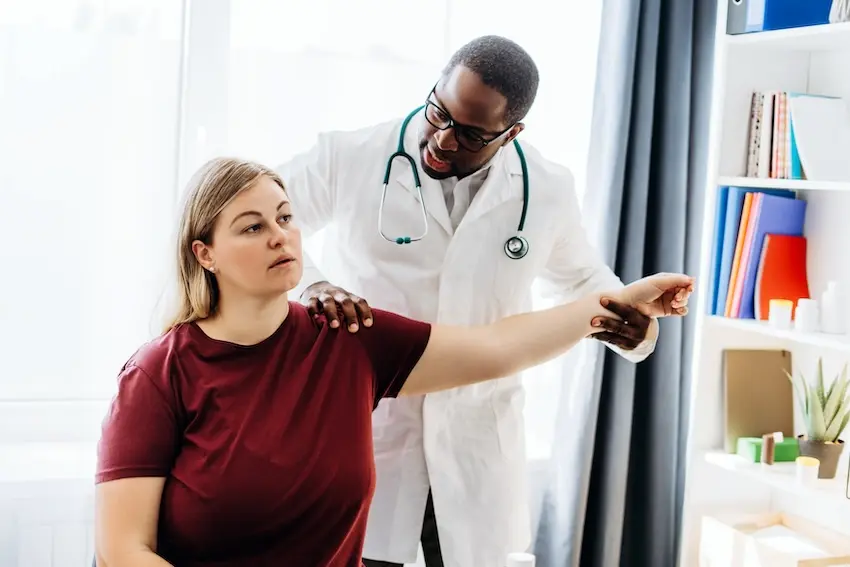 Car accident victim describing delayed whiplash and soft tissue pain symptoms to doctor at Atlanta urgent care facility