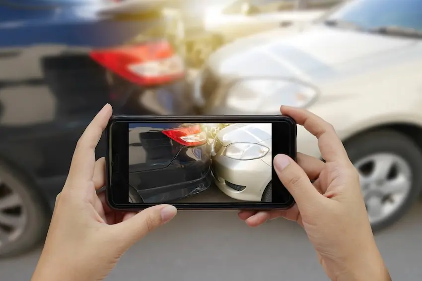 Car accident victim documenting vehicle damage with a smartphone at the scene of an Atlanta car accident