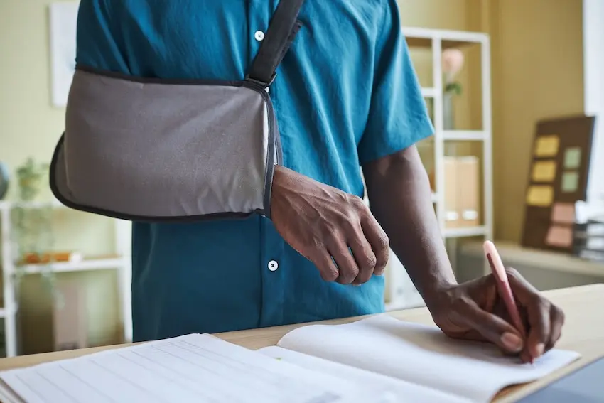 Car accident victim writing daily injury journal at home to document pain and physical limitations for Georgia personal injury claim